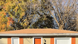 A single-story house with a front door, two windows with shutters, a small porch, and a well-maintained lawn.