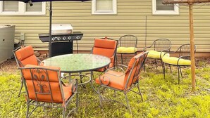 An outdoor patio with a round table and chairs, a barbecue grill, and a pergola.