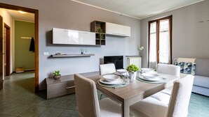 Ein modernes Wohnzimmer mit Esstisch für vier Personen, einer Couch, einem Fernseher und einer Einbauschränke mit einer Pflanze.