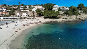 A beach with clear shallow waters, a sandy shore, and buildings in the background.
