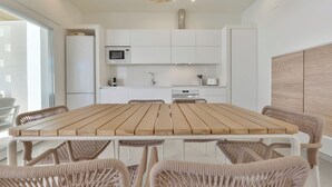 A modern kitchen with white cabinetry, a wooden dining table, wicker chairs, and a unique ceiling light fixture.