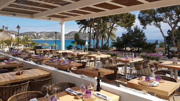 An outdoor café with tables and chairs, overlooking a coastal view.