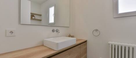 A modern bathroom with a white sink, wooden vanity, a large mirror, and a radiator.