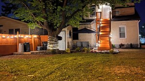 A residential area at night with a large tree, a house with a visible staircase, and a well-lit front yard. - Near Airport & Major Attractions, 5Mi Downtown, Comfy Loft (Louisville)