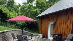 A patio area with a stone fire pit, outdoor seating, and a wooden building.
