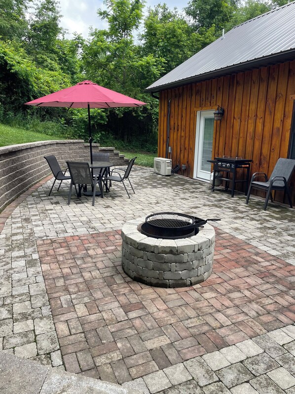 A patio area with a stone fire pit, outdoor seating, and a wooden building.