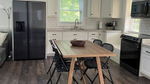A modern kitchen with white cabinets, a stainless steel refrigerator, a wooden dining table with chairs, and a black oven.