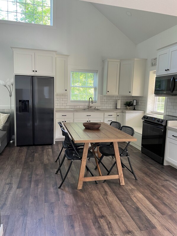 Una cocina moderna con armarios blancos, un refrigerador de acero inoxidable, una mesa de comedor de madera con sillas y un horno negro.