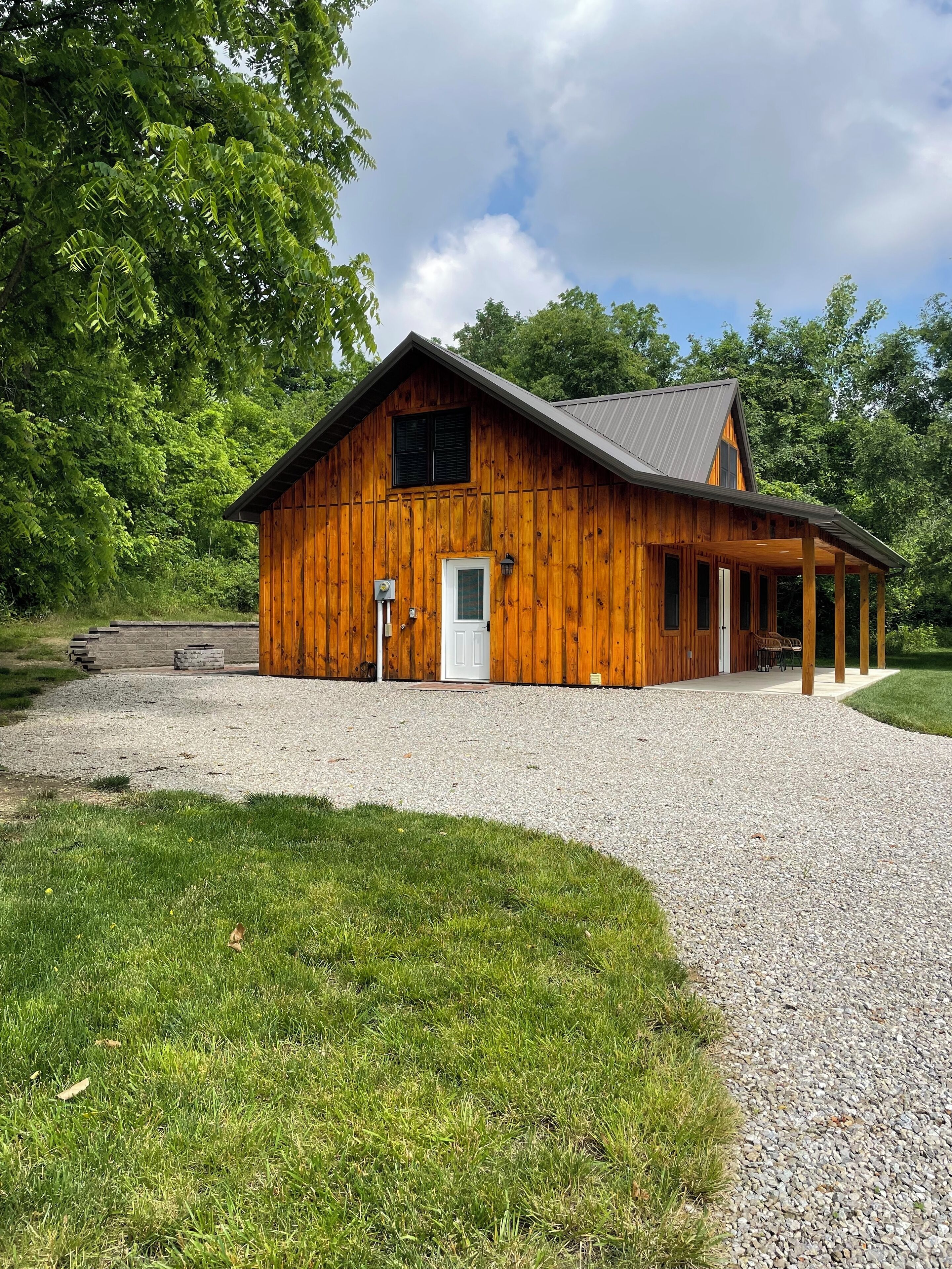 A wooden cabin with a gravel driveway and a covered porch.