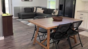 A modern kitchen with a large refrigerator, a dining table with chairs, and a gray sofa in the background.