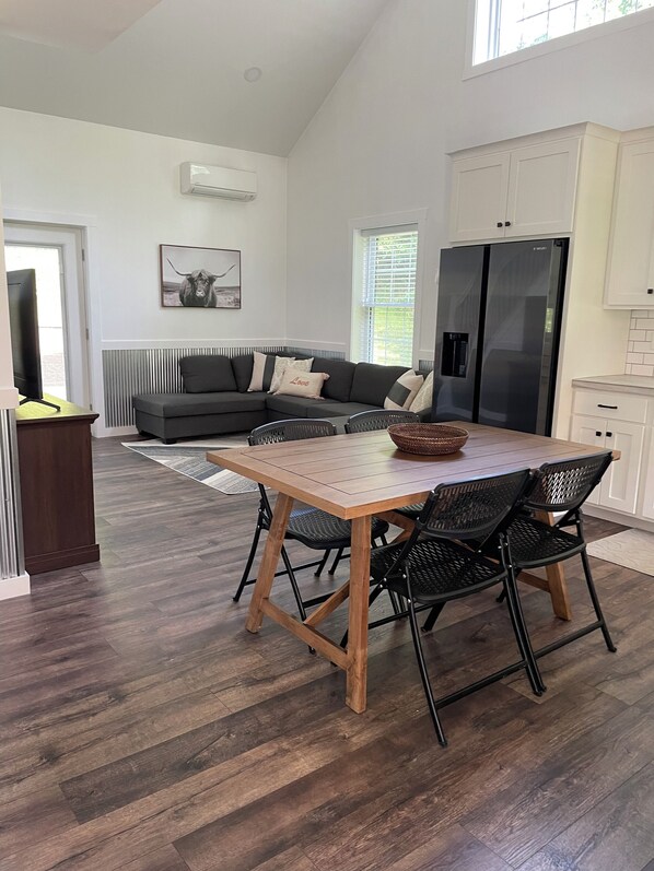 Una cocina moderna con un refrigerador grande, una mesa de comedor con sillas y un sofá gris al fondo.