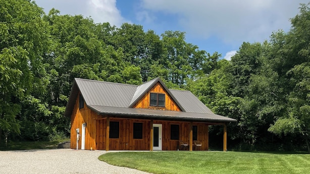 A wooden cabin with a metal roof, surrounded by a well-maintained lawn and dense trees.