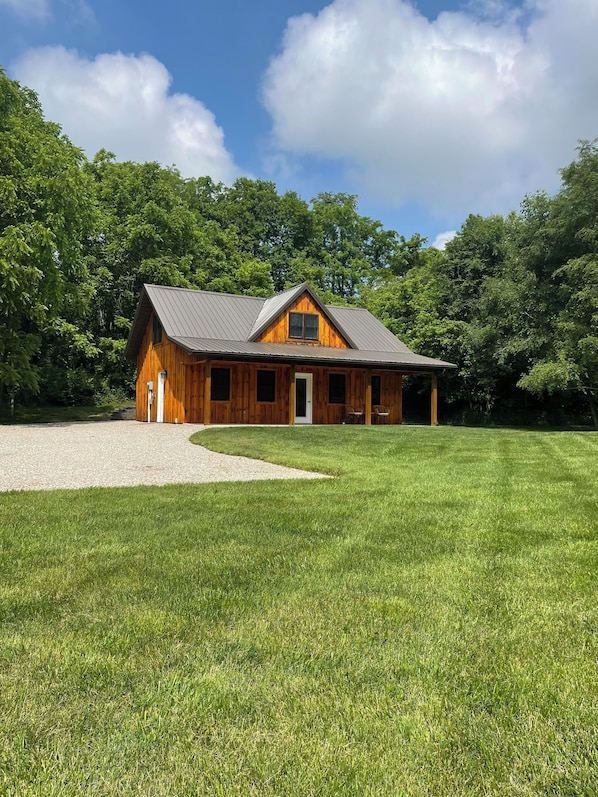 A wooden cabin with a metal roof, surrounded by a well-maintained lawn and dense trees.
