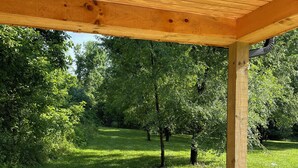 A covered outdoor area with a concrete floor, surrounded by a grassy field and trees.