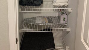 A storage closet with multiple shelves, some holding folded towels and blankets, and a box on the bottom shelf.