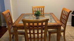 A dining area with a glass-top table surrounded by four wooden chairs with intricate back designs.