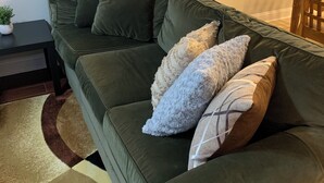 A green sofa with multiple cushions, a small table with a plant, and a patterned rug.