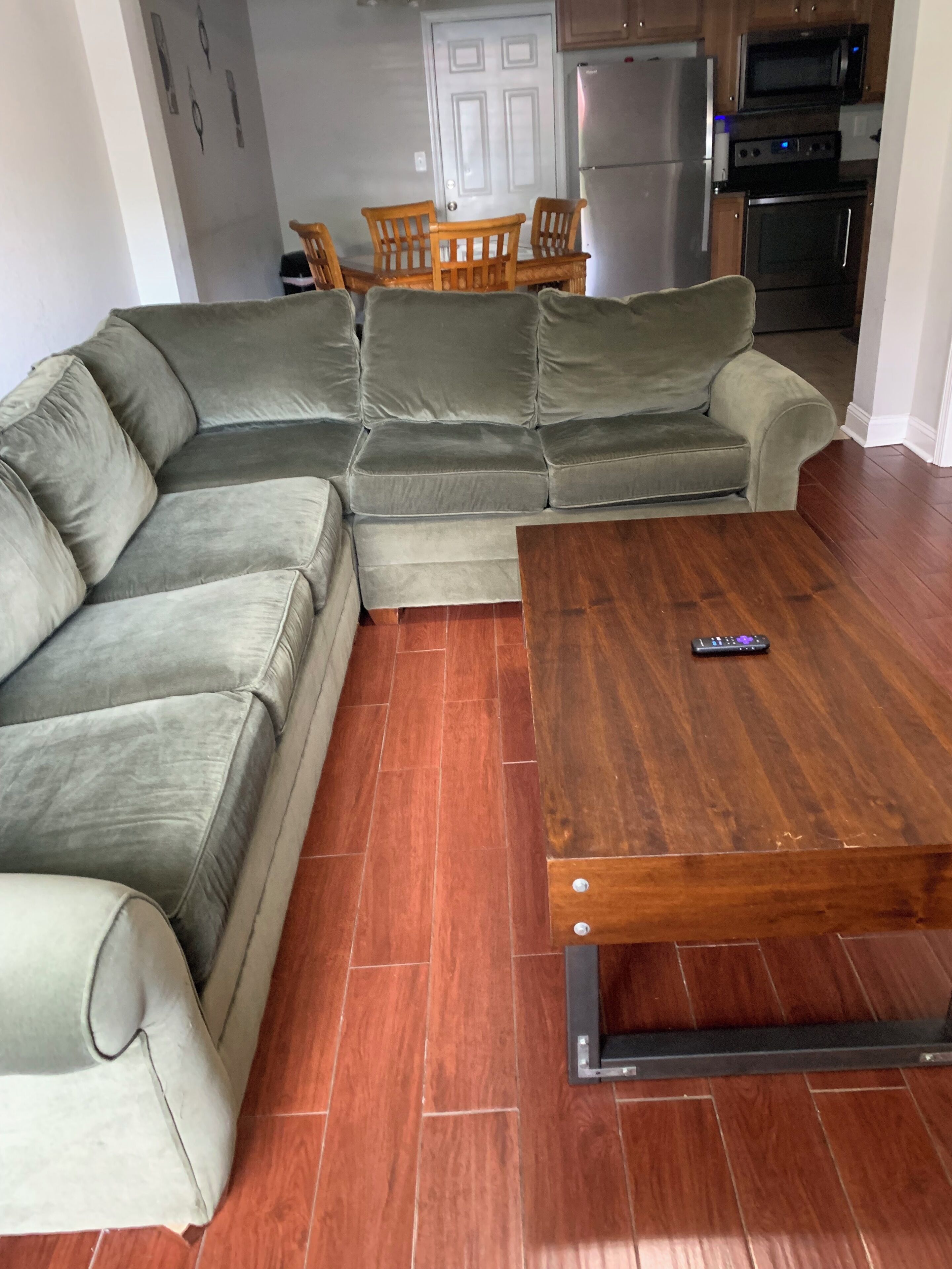 A living room with a sectional sofa, a wooden coffee table, and a kitchen in the background.