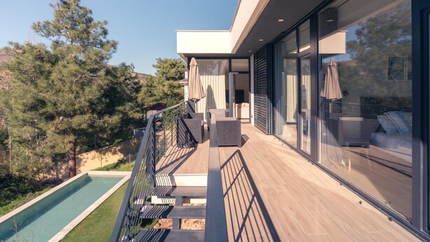 Un balcón moderno al aire libre con piscina, terraza de madera y puertas de vidrio que dan a un área de estar.