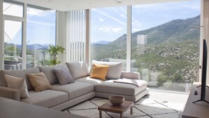Una sala de estar moderna con un amplio sofá modular, una mesa de centro y vistas a un paisaje montañoso a través de grandes ventanales.
