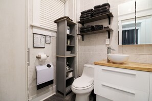 Un baño moderno con inodoro, lavamanos de cuenca grande, repisas con toallas y un espejo sobre el lavamanos.