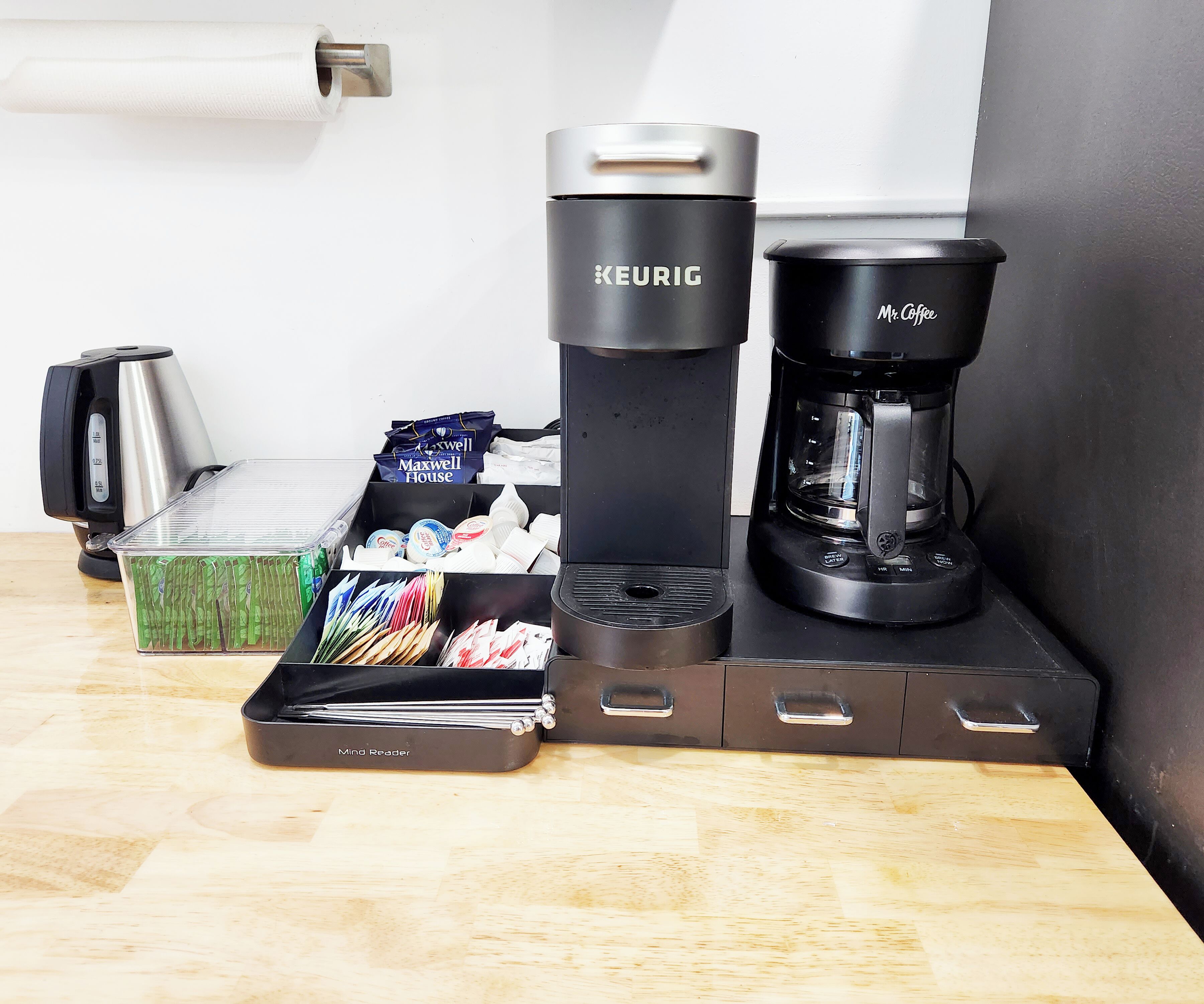 A coffee maker, a kettle, and a coffee pot on a wooden table.