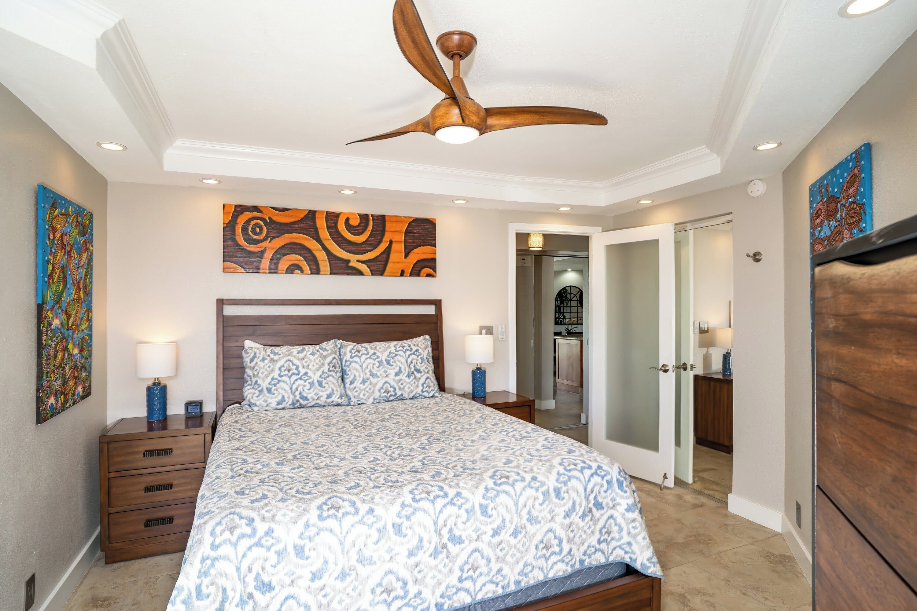 Un dormitorio con una cama grande, un ventilador de techo y obras de arte en las paredes.