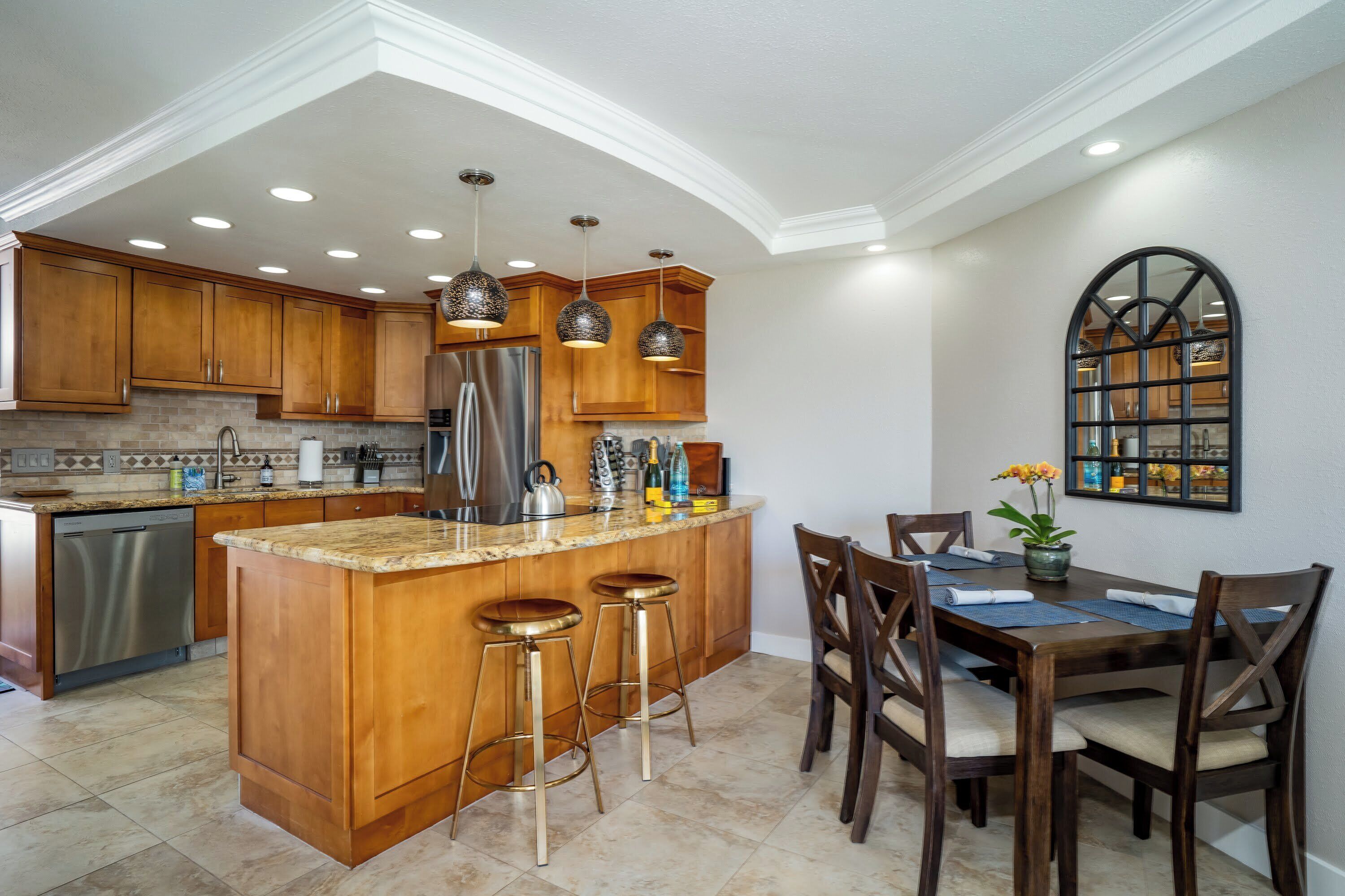 A kitchen with wooden cabinets, a stainless steel refrigerator, and a bar area with stools.