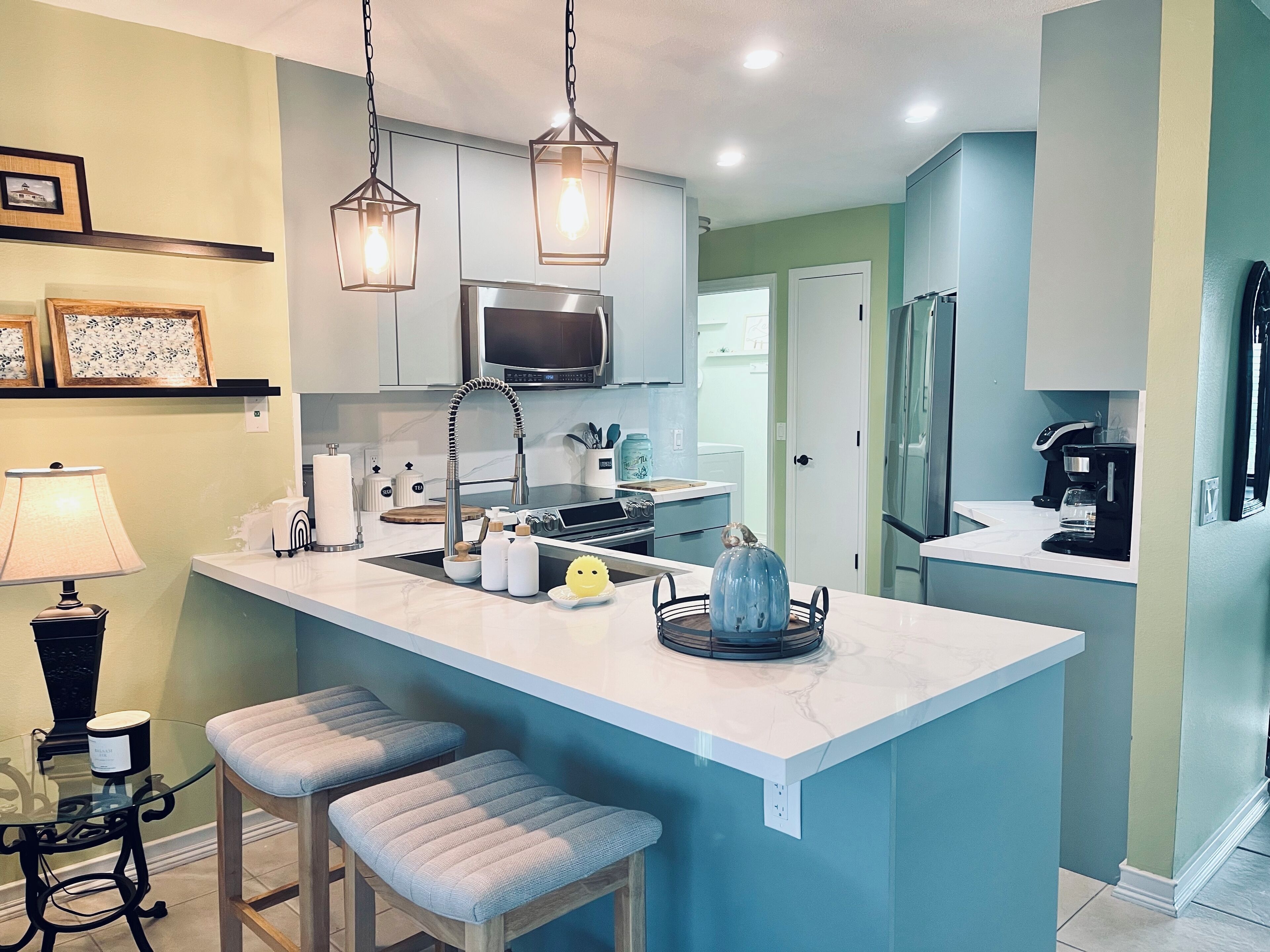 A modern kitchen with a central island, bar stools, pendant lighting, and a refrigerator.