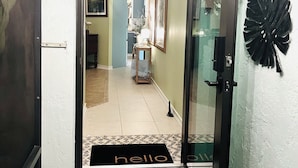 Un couloir avec une pancarte « BIENVENUE », un paillasson sur lequel est écrit « bonjour » et une feuille noire décorative accrochée au mur.
