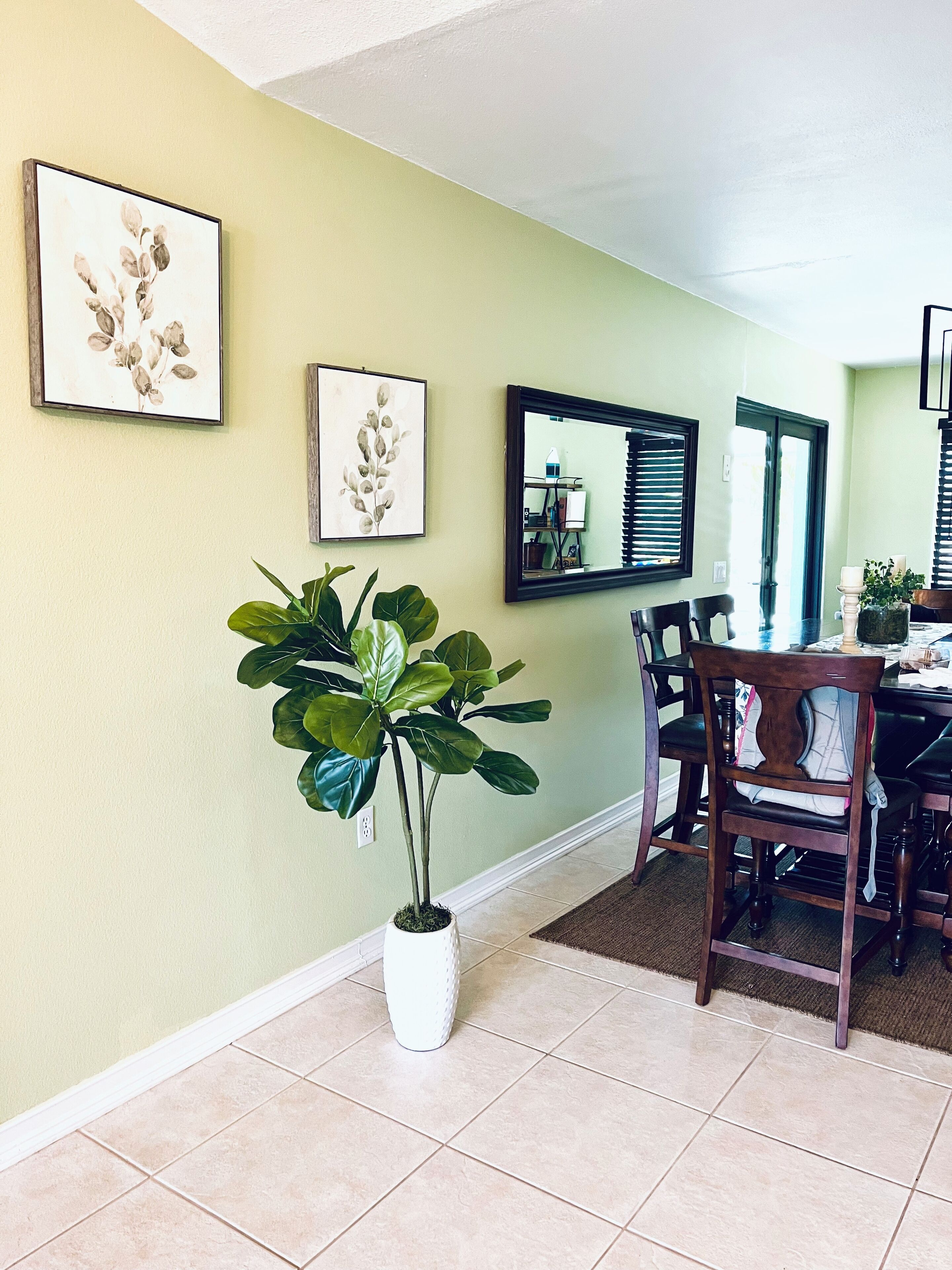 Un coin repas avec une table et des chaises, une plante en pot et des œuvres d’art encadrées accrochées au mur.