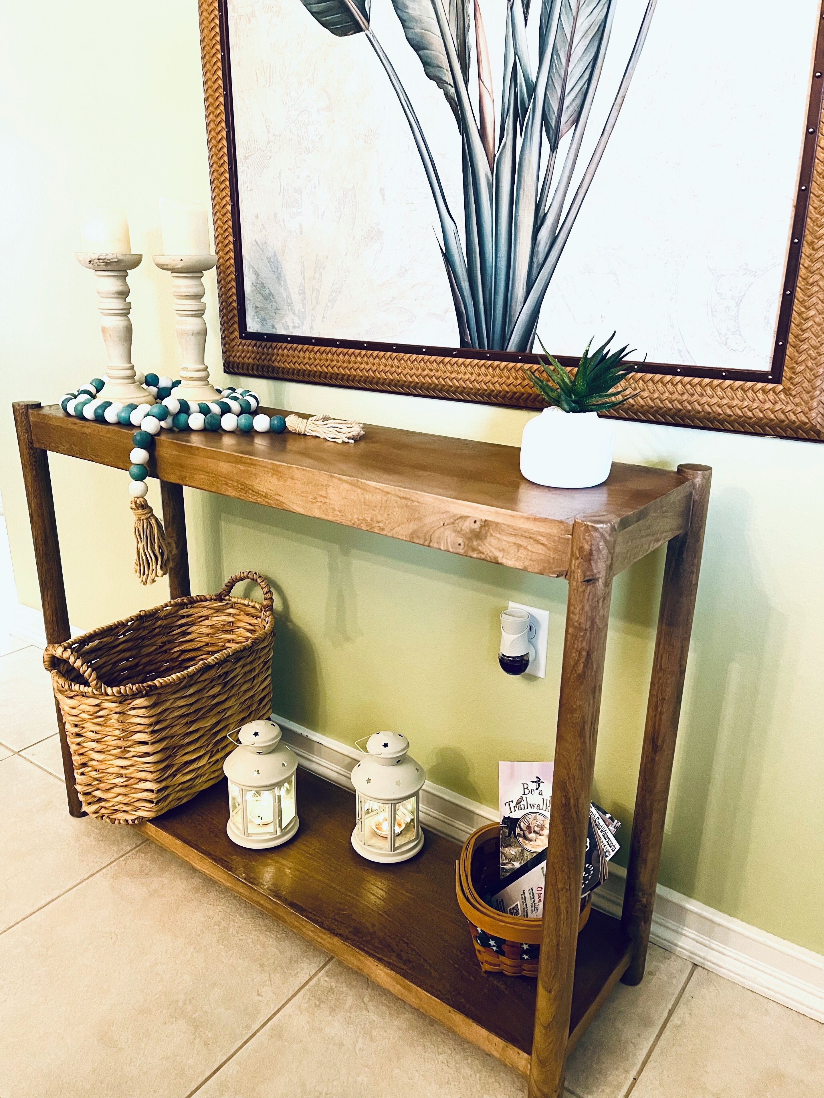 A wooden console table with a woven basket, two lanterns, and a small potted plant.