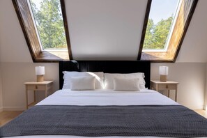 A bedroom with a skylight, a bed with white bedding, two bedside tables with lamps, and a dark headboard. - Emberwood Lodge - Luxury Cabin, Kid Friendly (Catskill)