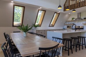A modern kitchen with a wooden dining table, black chairs, and a central island with stools. - Emberwood Lodge - Luxury Cabin, Kid Friendly (Catskill)