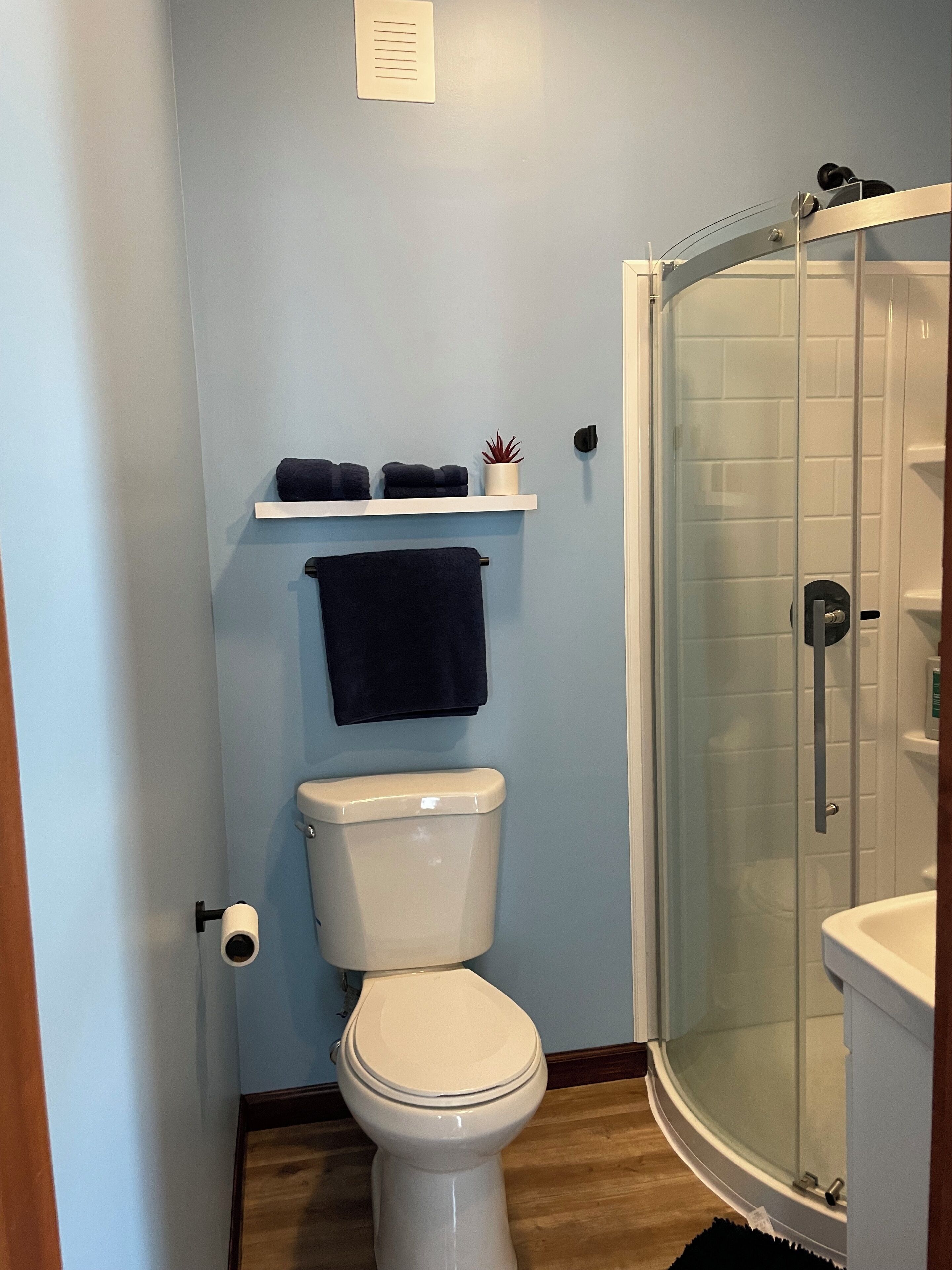 Een badkamer met een toilet, een plank met handdoeken en een douche met glazen wanden.