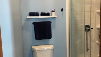 A bathroom with a toilet, a shelf with towels, and a glass-enclosed shower.