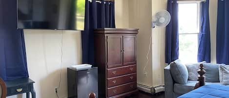 Un dormitorio con cama, cómoda, televisor montado en la pared y ventana con cortinas.