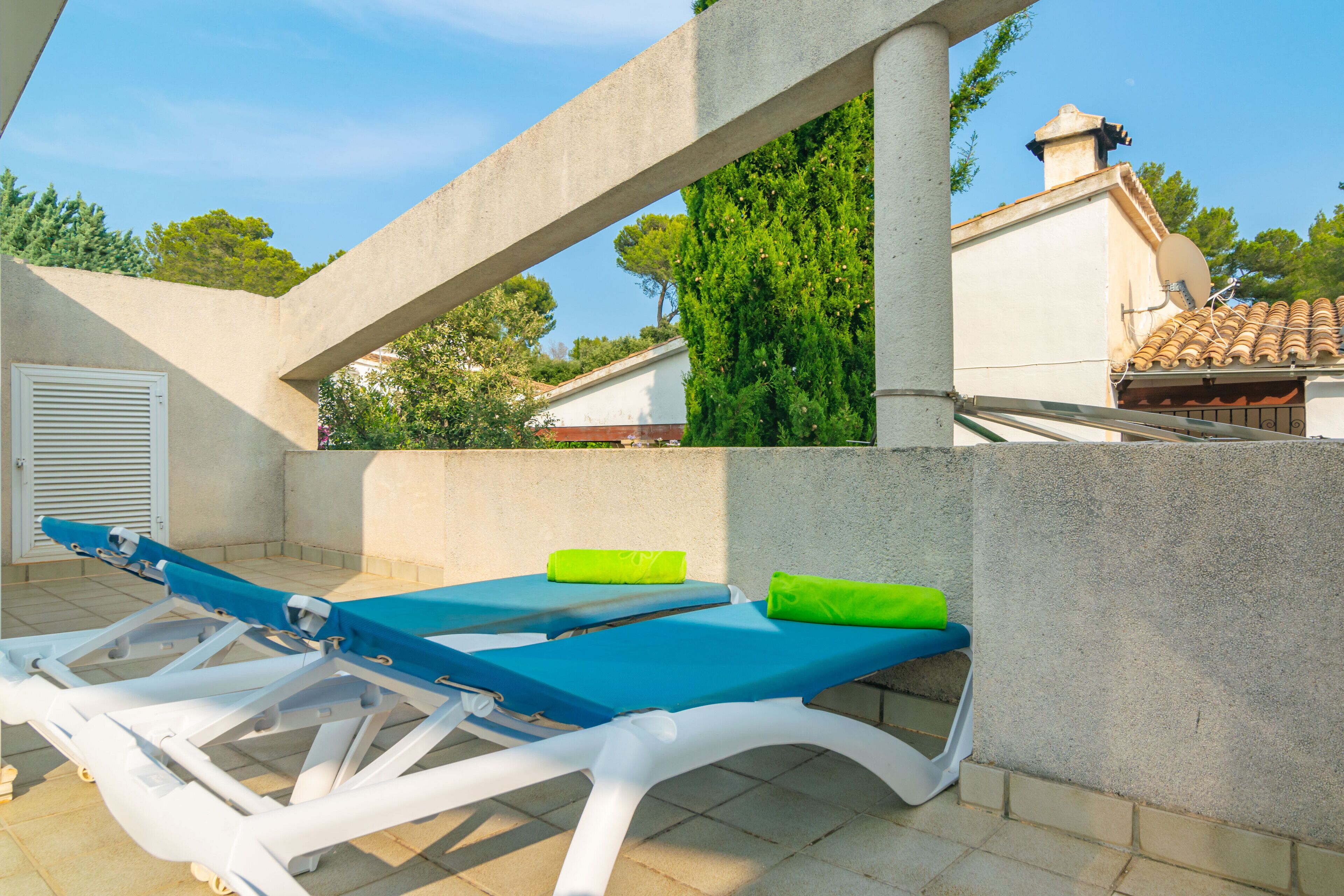 A rooftop terrace with two lounge chairs, one with a blue cushion and the other with a green cushion, and a white wall in the background.
