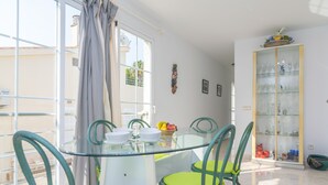 Un comedor con una mesa y sillas de vidrio, una ventana con cortinas, y un aparador de vidrio con objetos decorativos.