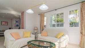 Una sala de estar con dos sofás blancos, una mesa de centro de vidrio y una lámpara.