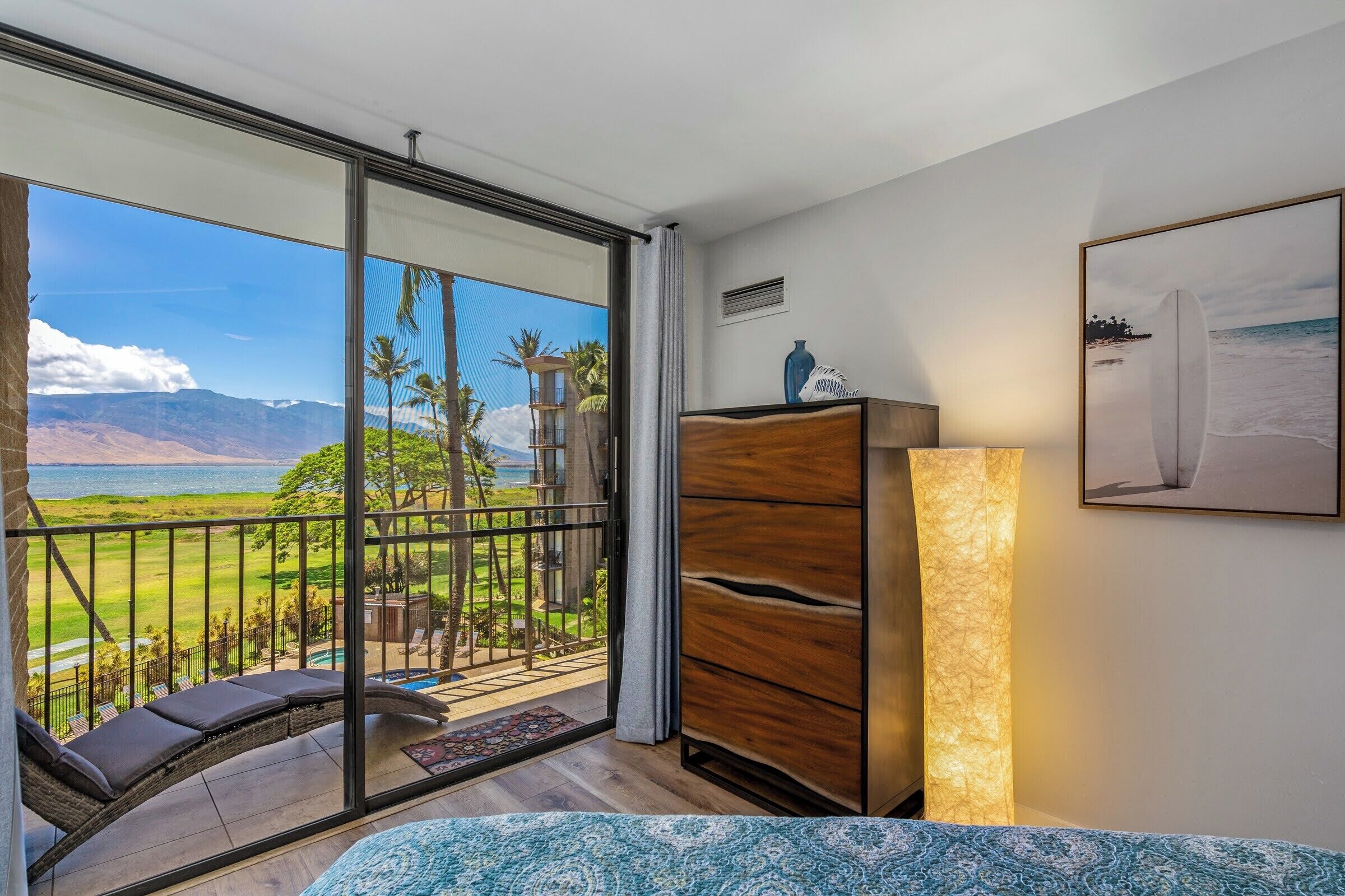 Uma varanda com vista para montanhas e piscina, um aparador de madeira e uma cama com colcha estampada.