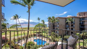 A balcony with wicker furniture, a pool, and a view of a beach and mountains. - Modern and Relaxing Oceanfront Vistas (Kihei)