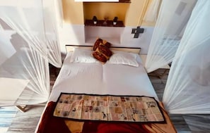 Una cama bien tendida con sábanas blancas, un plaid decorativo y una mesita con una revista.