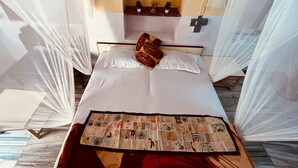 A bed with white linens, a quilt, and a pillow with a red and gold pattern. - Berozgar Hostel (Jaisalmer)