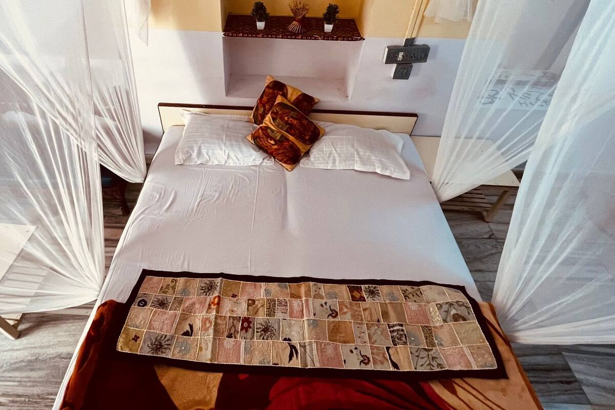 A bed with white linens, a quilt, and a pillow with a red and gold pattern.