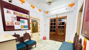 A room with a bed, two blue cushioned chairs, a wooden cabinet, a bulletin board, and a window with curtains. - Berozgar Hostel (Jaisalmer)