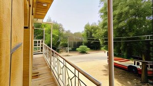 A wooden deck with a metal railing overlooking a dirt path and a red vehicle. - Berozgar Hostel (Jaisalmer)