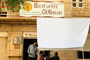 Un bâtiment avec une enseigne sur laquelle on peut lire « Berajaigar Chaiwala » et une tente blanche installée devant.