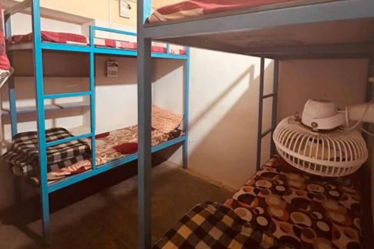 A bunk bed room with a white fan on the lower bunk and a checkered blanket on the upper bunk.