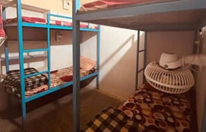 Une chambre avec un lit superposé, un ventilateur blanc sur le lit du bas et une couverture à carreaux sur le lit du haut.